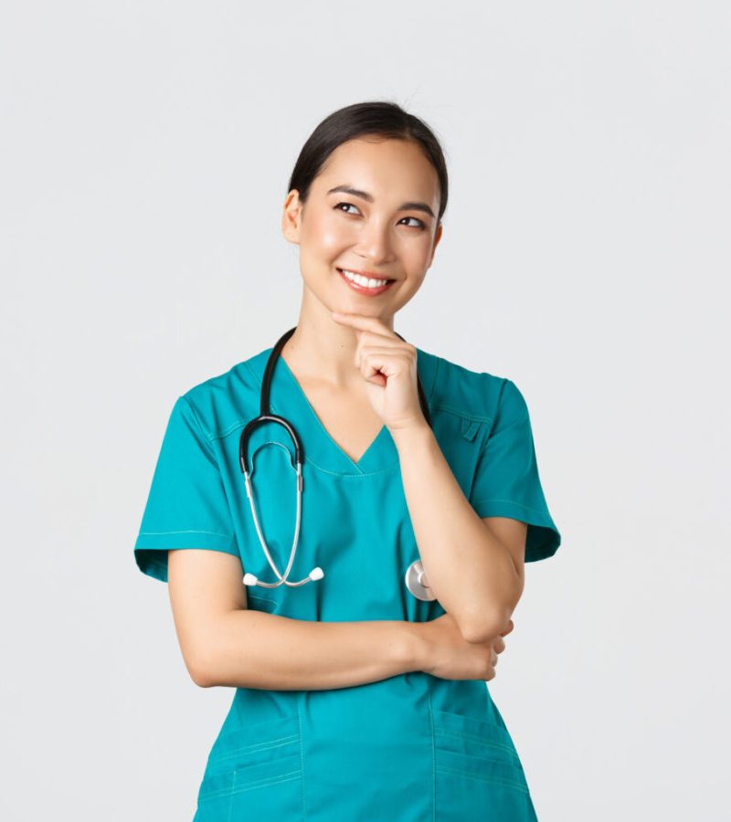 Covid-19, healthcare workers, pandemic concept. Smiling pleased attractive asian female doctor in scrubs, looking upper left corner and thinking, have idea, standing thoughtful white background.